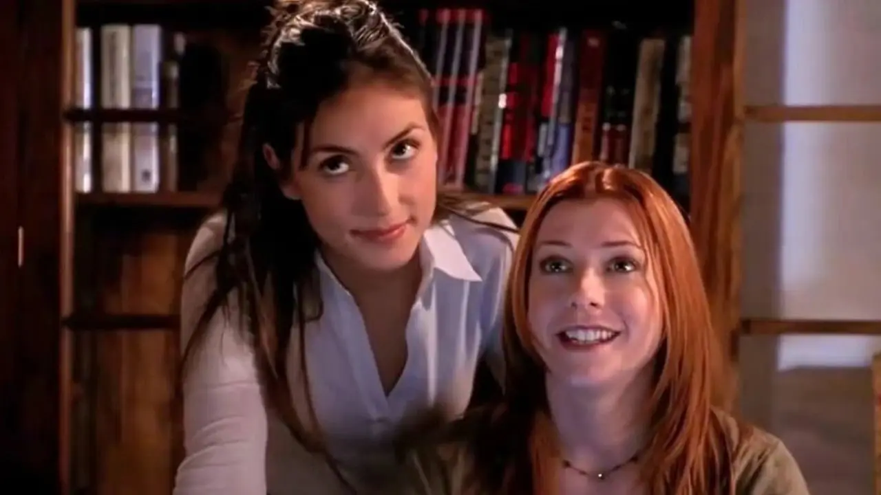 Kennedy se inclina sobre el hombro de Willow mientras Willow está sentada en su escritorio en la temporada 7 de Buffy, la cazavampiros. Kennedy se inclina sobre el hombro de Willow mientras Willow está sentada en su escritorio en la temporada 7 de Buffy, la cazavampiros.