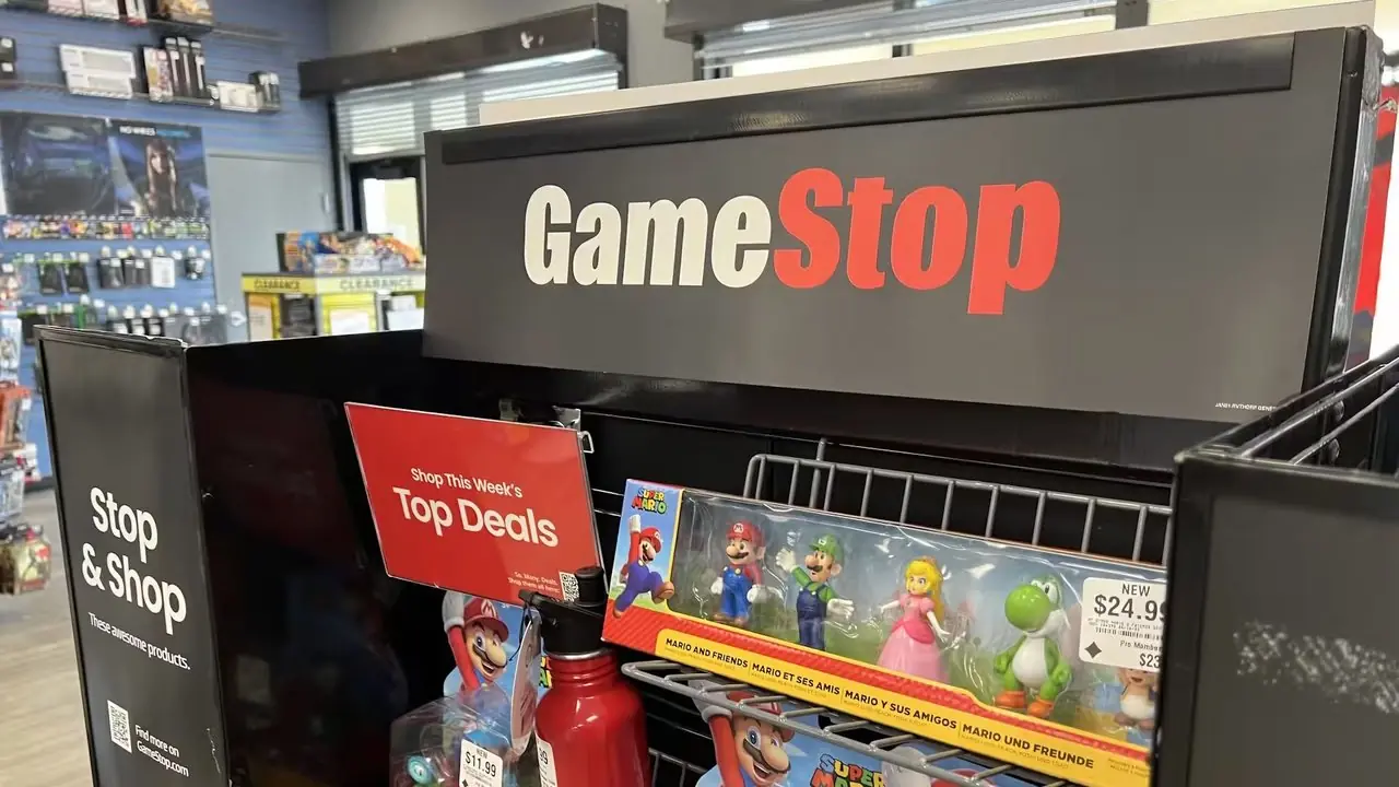 Ett GameStop-skyltfönster under normala öppettider, med annonser för flera spel och konsoler.