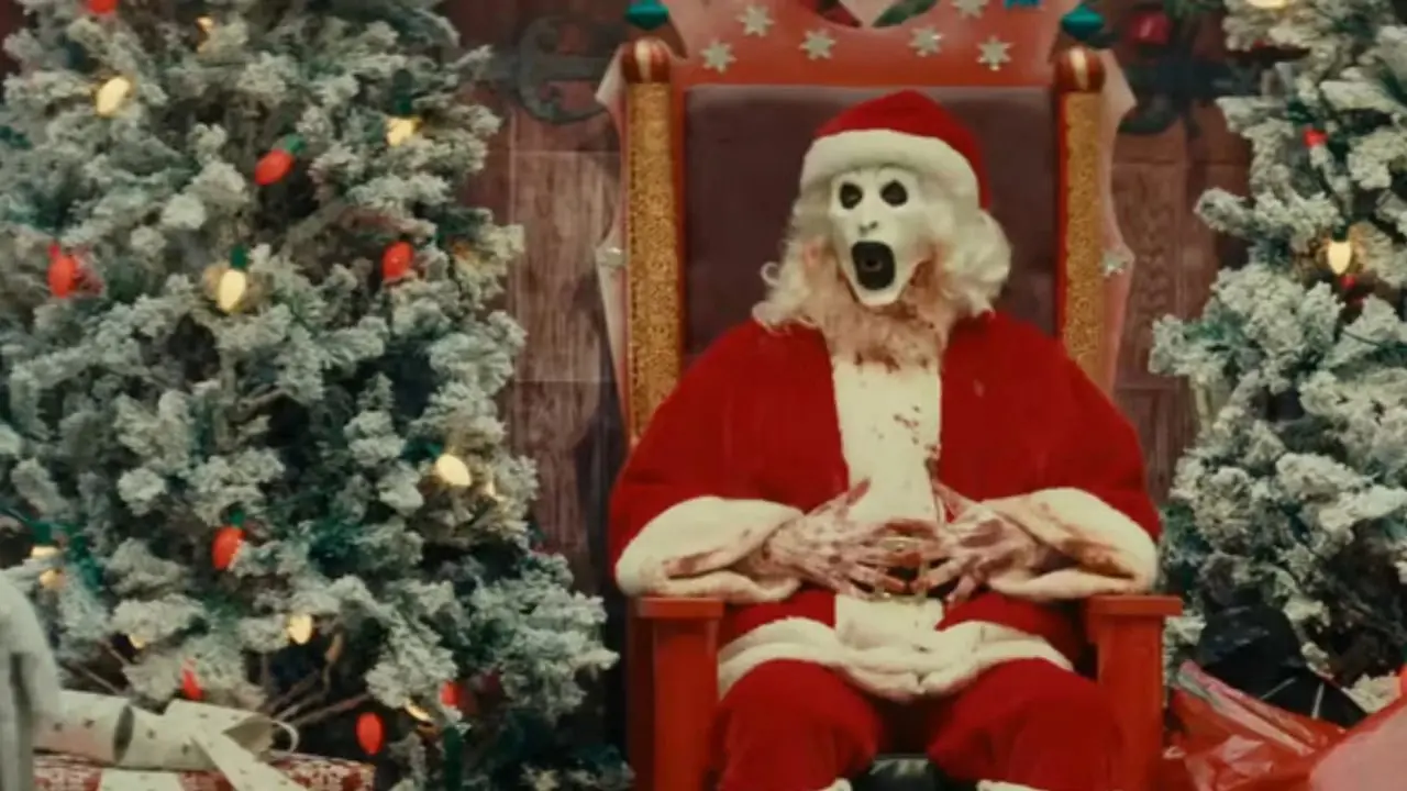 Art the Clown como Santa sonriendo mientras sostiene un hacha en Terrifier 3